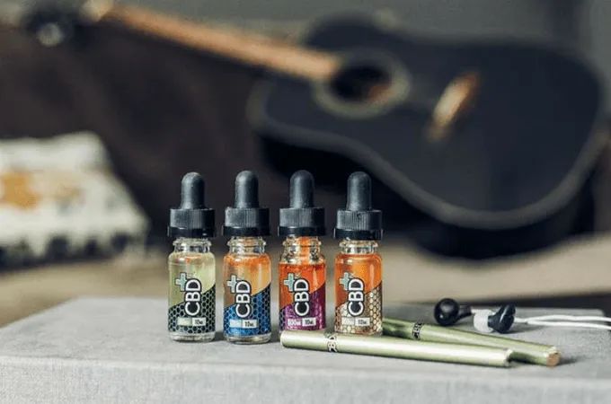 Four CBDfx vape oil bottles and a vape pen beside an acoustic guitar