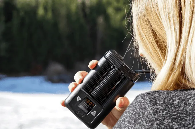 A hand holding a black Mighty vaporizer outdoors against snow